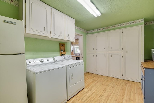 washroom featuring cabinet space, a textured ceiling, light wood-style flooring, and washing machine and clothes dryer
