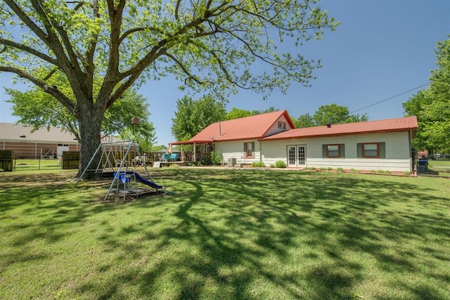 rear view of house featuring a playground, fence, a lawn, and metal roof
