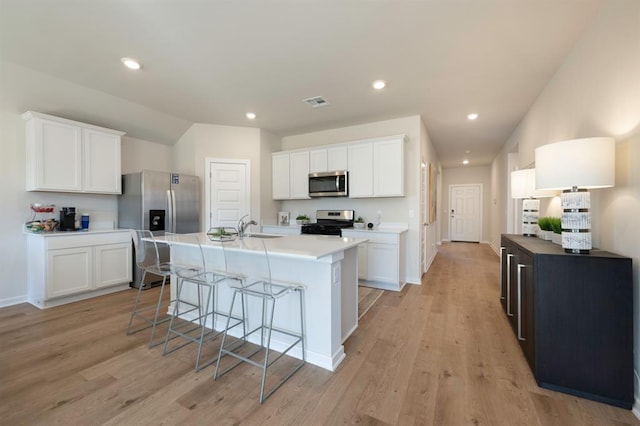 kitchen with a kitchen breakfast bar, stainless steel appliances, light wood-type flooring, and white cabinetry