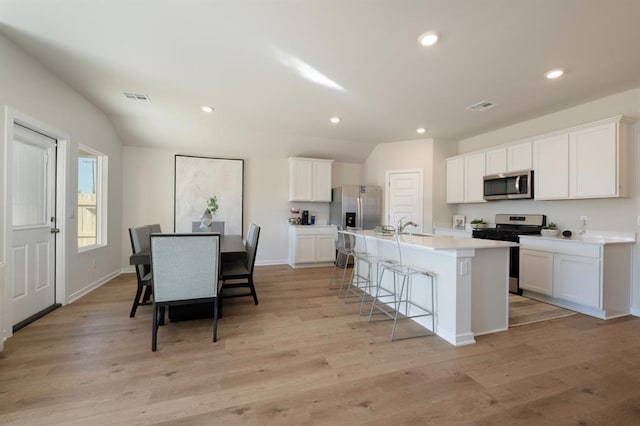 kitchen with appliances with stainless steel finishes, a breakfast bar, visible vents, an island with sink, and vaulted ceiling