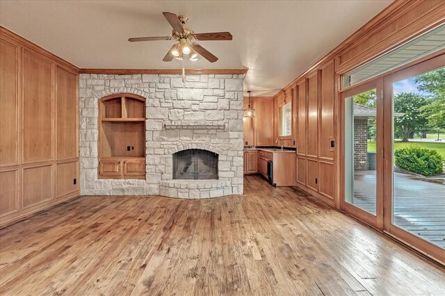 1008 Bavarian Dr, Edmond, OK 73034 - unfurnished living room featuring light wood-style floors, a stone fireplace, ceiling fan, ornamental molding, and built in features