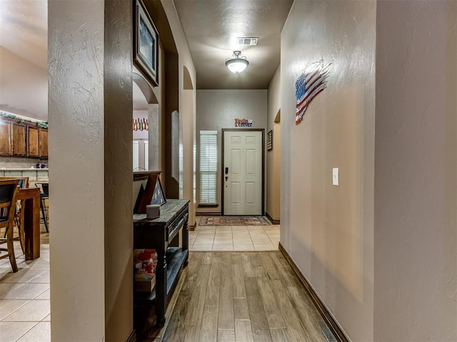 doorway featuring arched walkways, a textured wall, and visible vents