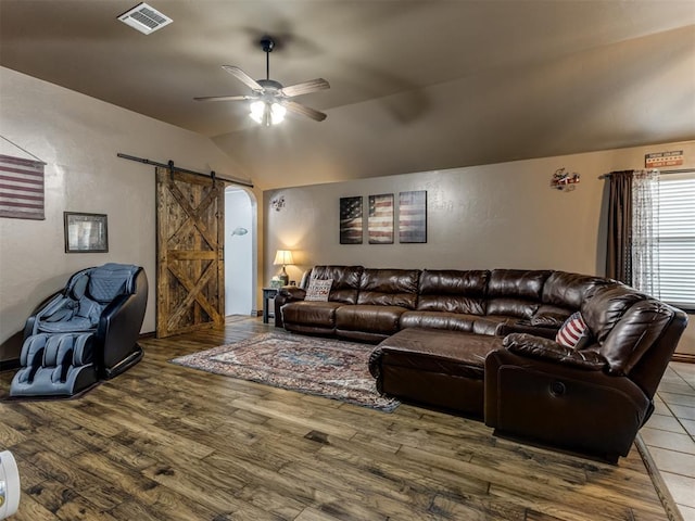 living room with ceiling fan, a barn door, light wood-style floors, lofted ceiling, and visible vents