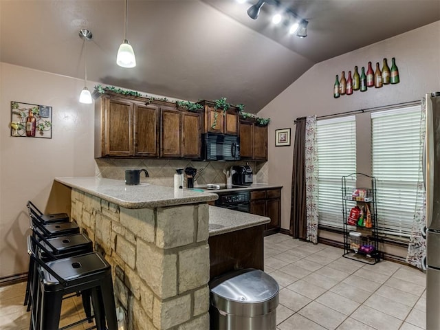 kitchen with decorative backsplash, black microwave, vaulted ceiling, light tile patterned floors, and a peninsula