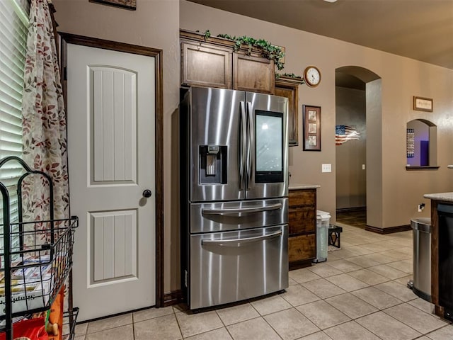 kitchen with arched walkways, baseboards, stainless steel fridge, and light tile patterned floors