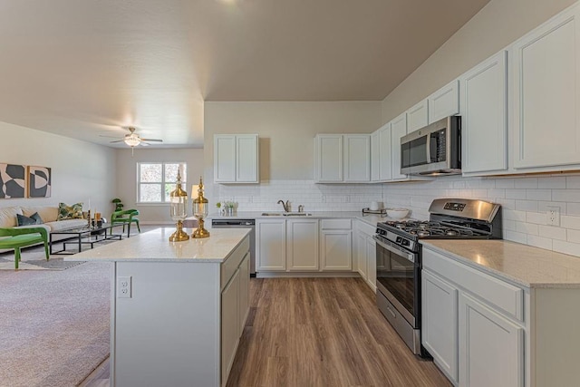 kitchen featuring appliances with stainless steel finishes, a center island, wood finished floors, a sink, and open floor plan