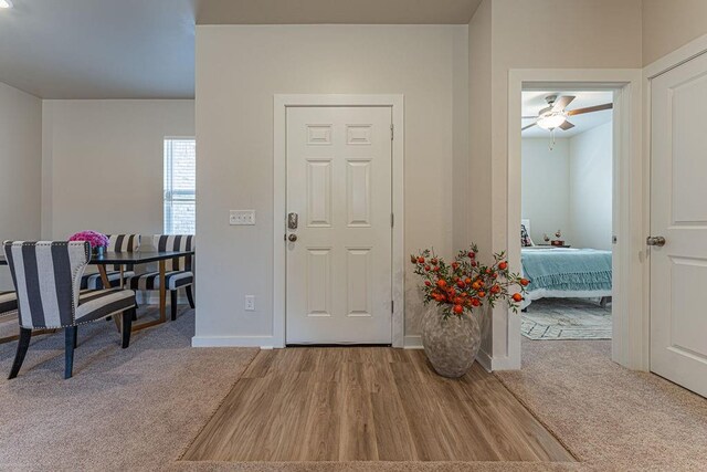 carpeted entrance foyer featuring a ceiling fan, baseboards, and wood finished floors