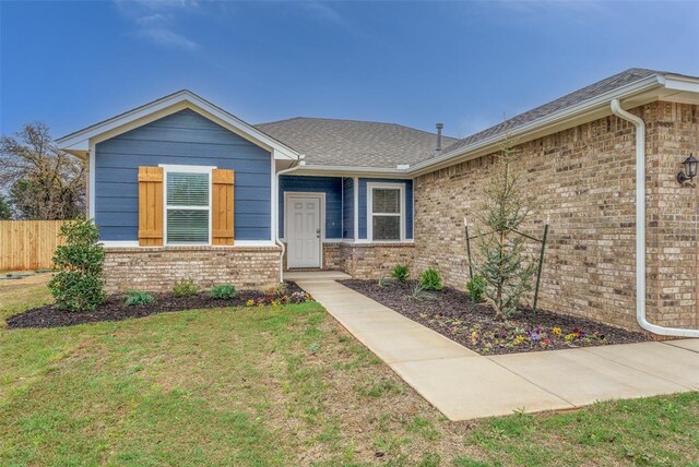 ranch-style home featuring brick siding, fence, a shingled roof, and a front lawn