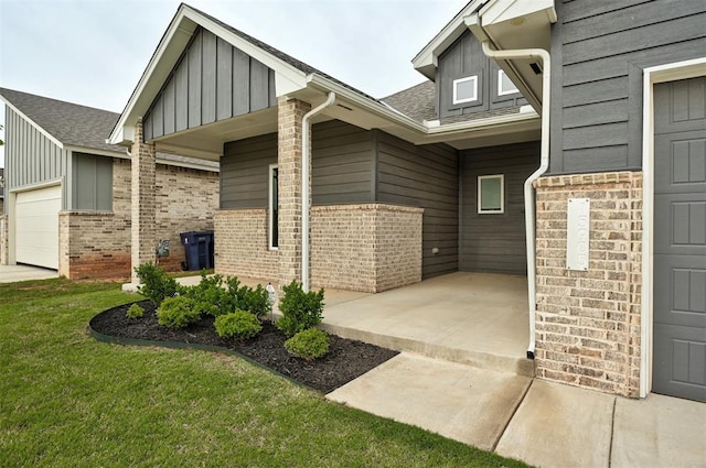 doorway to property featuring board and batten siding, brick siding, an attached garage, and a yard