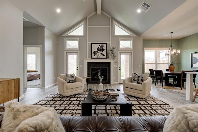 living area with a chandelier, a fireplace, light wood-style flooring, plenty of natural light, and high vaulted ceiling