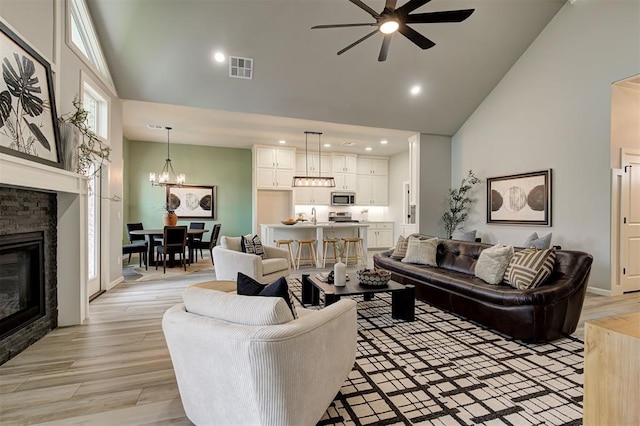 living area with high vaulted ceiling, ceiling fan, a stone fireplace, recessed lighting, and a chandelier