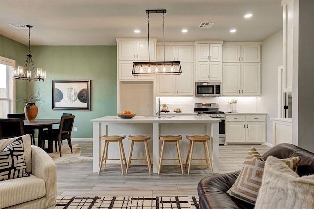kitchen with appliances with stainless steel finishes, open floor plan, a chandelier, a sink, and white cabinets