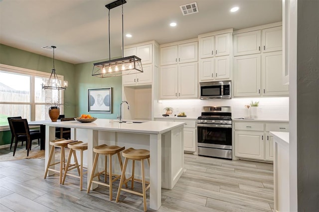 kitchen featuring stainless steel appliances, a sink, backsplash, white cabinetry, and light countertops