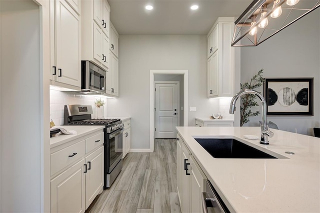 kitchen with stainless steel appliances, a sink, light countertops, recessed lighting, and white cabinetry