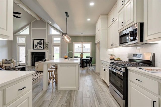 kitchen featuring stainless steel appliances, a sink, open floor plan, a fireplace, and light countertops