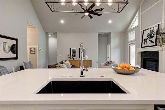 kitchen featuring open floor plan, high vaulted ceiling, a sink, pendant lighting, and a glass covered fireplace
