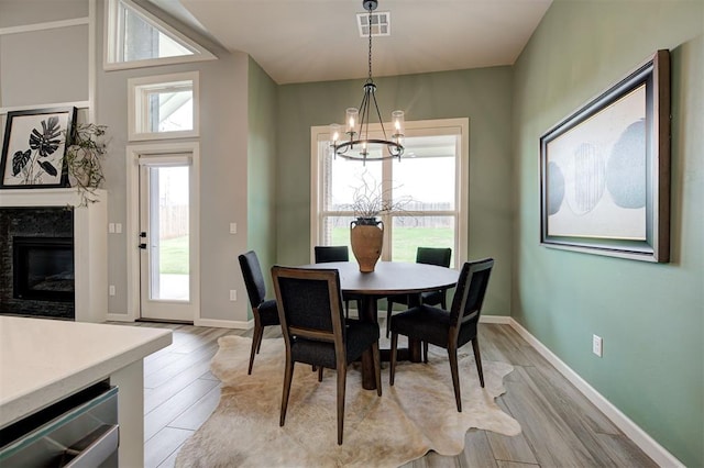 dining room with a chandelier, a high end fireplace, light wood-style floors, and baseboards