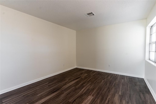 spare room featuring baseboards, visible vents, a textured ceiling, and dark wood-type flooring