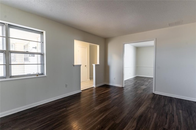unfurnished room with baseboards, dark wood finished floors, a textured ceiling, and visible vents
