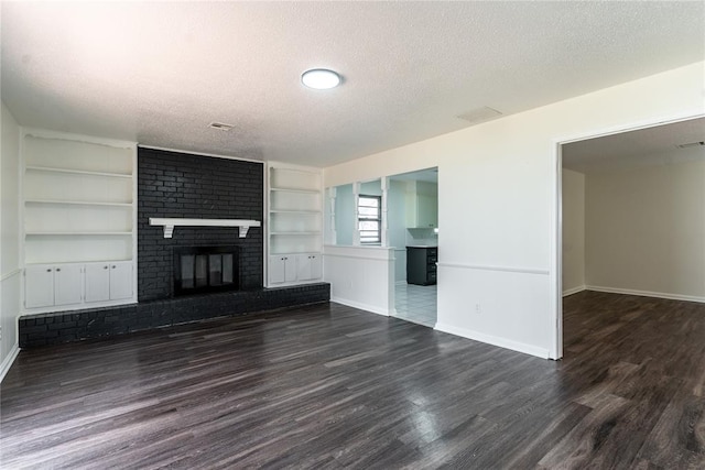 unfurnished living room featuring a brick fireplace, a textured ceiling, dark wood finished floors, built in shelves, and baseboards