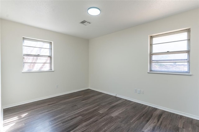 empty room featuring baseboards, dark wood-style floors, and visible vents