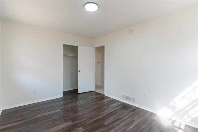 unfurnished bedroom featuring a closet, baseboards, dark wood-type flooring, and visible vents