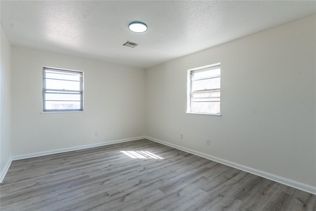 spare room featuring baseboards, a textured ceiling, wood finished floors, and visible vents