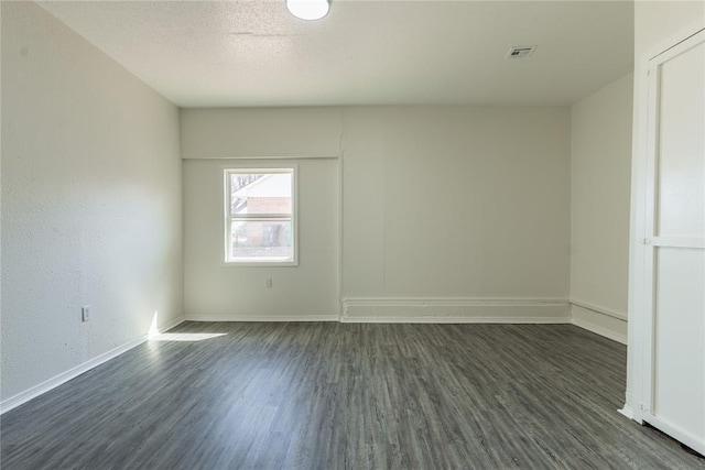 empty room featuring baseboards, visible vents, and dark wood-type flooring