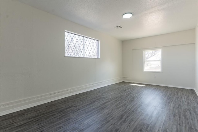 empty room featuring baseboards, dark wood-style flooring, a textured ceiling, and visible vents