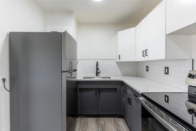 kitchen featuring appliances with stainless steel finishes, a sink, light wood finished floors, light countertops, and white cabinetry