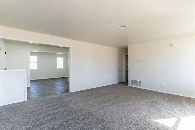 spare room featuring baseboards, dark colored carpet, and visible vents