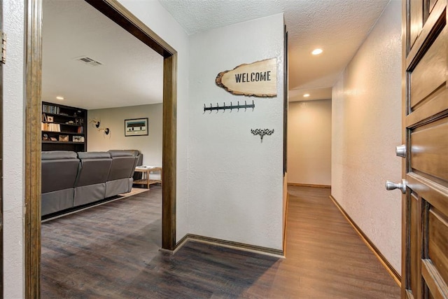 hallway with dark wood-style flooring, a textured ceiling, and visible vents