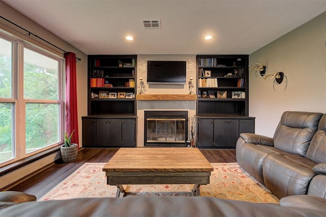 living area featuring baseboard heating, built in shelves, a large fireplace, wood finished floors, and visible vents