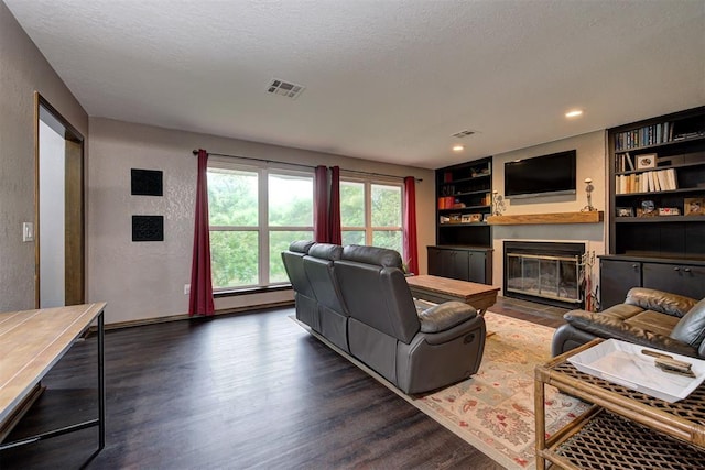 living room with built in shelves, visible vents, a fireplace with flush hearth, and dark wood finished floors