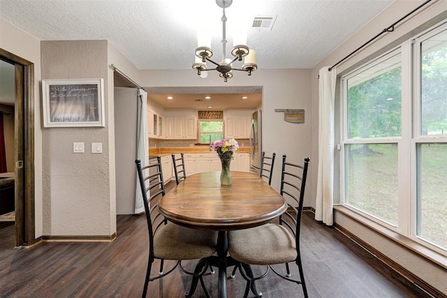 dining room with a notable chandelier, dark wood-type flooring, a textured ceiling, and visible vents