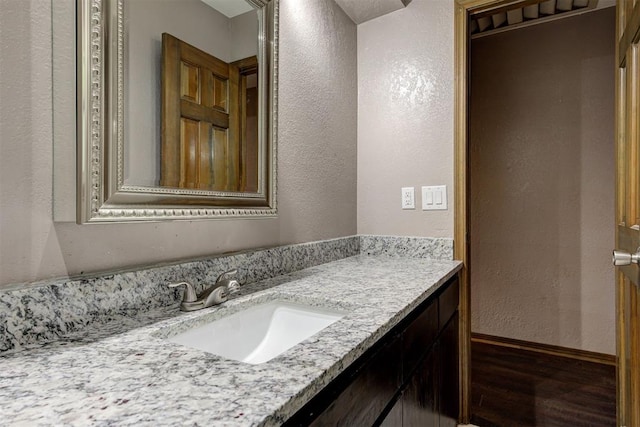 bathroom with vanity, a textured wall, baseboards, and wood finished floors