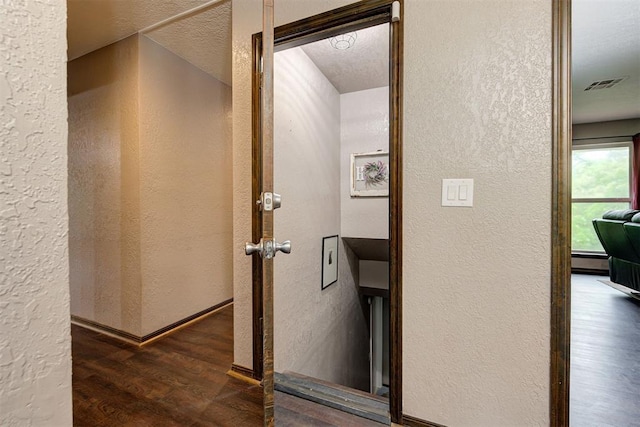 corridor with visible vents, a textured wall, and wood finished floors