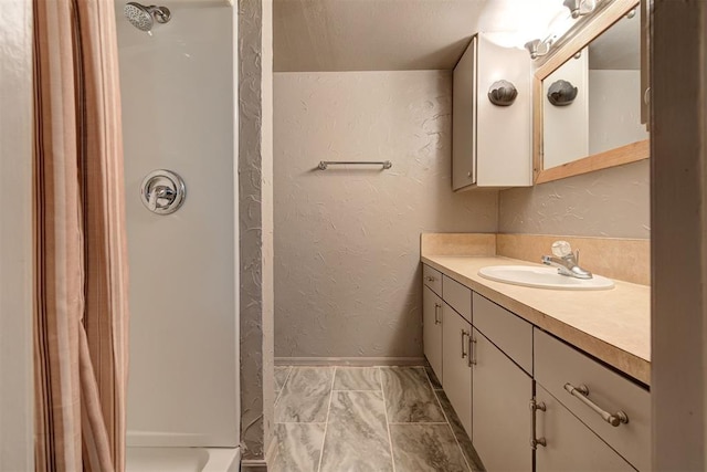 full bath featuring a shower with curtain, a textured wall, baseboards, and vanity