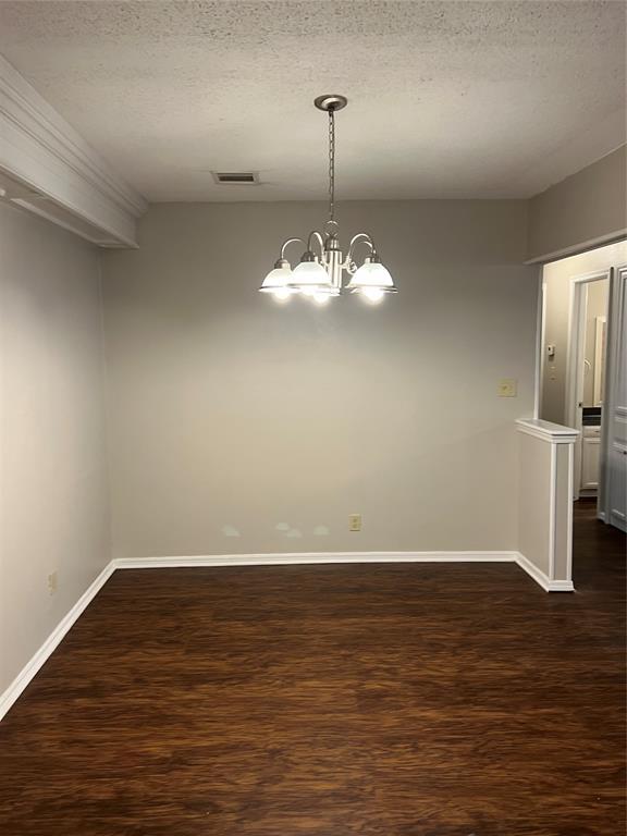 924 N Bradley Ave, Oklahoma City, OK 73127 - unfurnished dining area with a textured ceiling, visible vents, baseboards, an inviting chandelier, and dark wood-type flooring