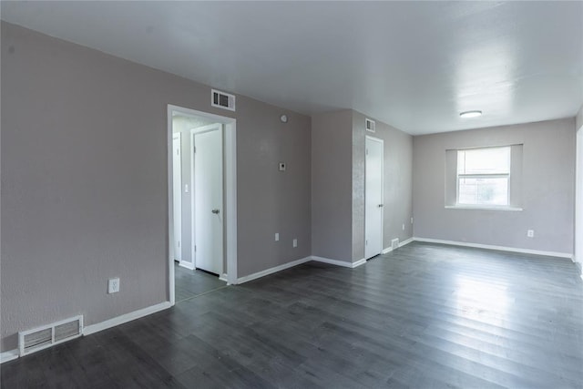empty room with baseboards, dark wood-style flooring, and visible vents