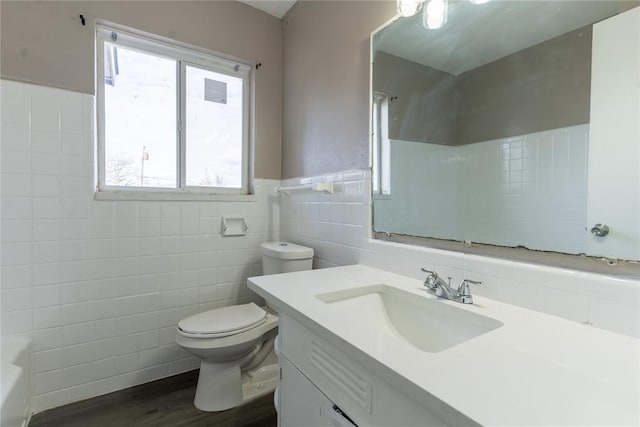 bathroom featuring tile walls, wood finished floors, a bathing tub, vanity, and toilet