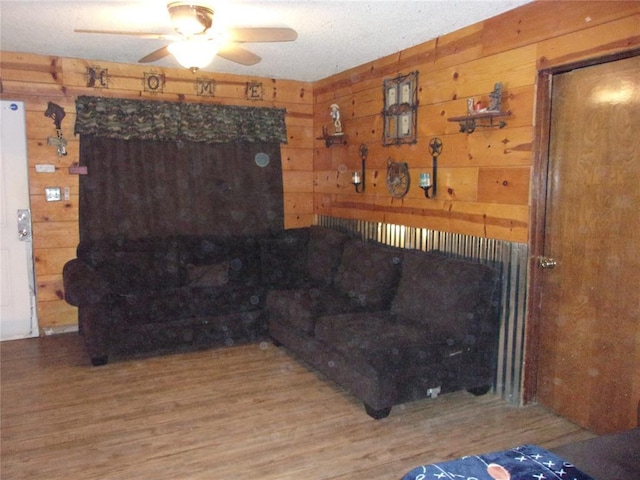 living room featuring light wood-type flooring, a ceiling fan, and wood walls
