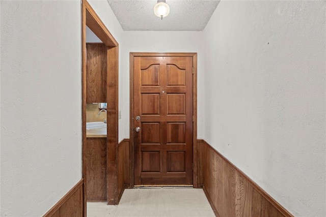entryway featuring wooden walls, a textured ceiling, a sink, and a wainscoted wall