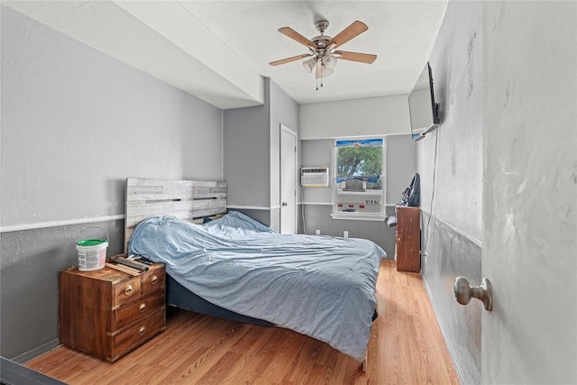 bedroom featuring a ceiling fan, a wall unit AC, and wood finished floors