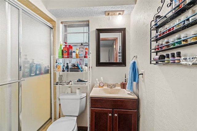 full bath featuring vanity, a textured wall, toilet, and a shower stall