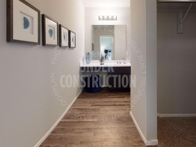 hall featuring a sink, baseboards, and wood finished floors