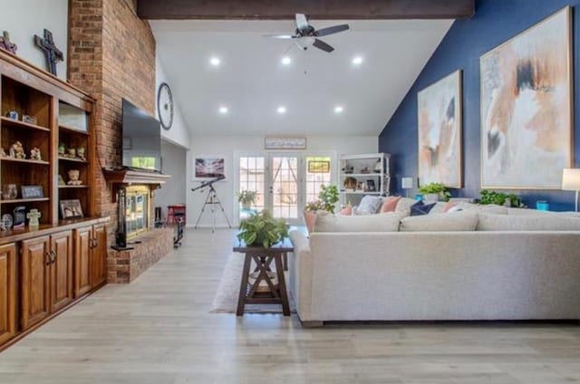 living area featuring ceiling fan, beam ceiling, light wood-style floors, a fireplace, and high vaulted ceiling