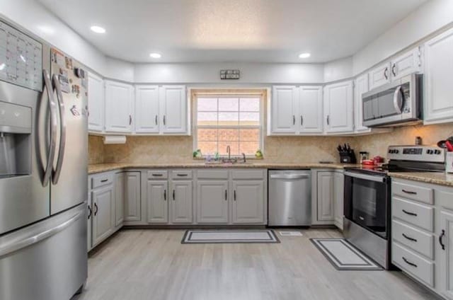 kitchen with white cabinets, appliances with stainless steel finishes, a sink, light wood finished floors, and tasteful backsplash