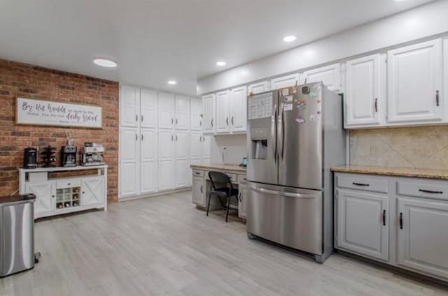 kitchen with stainless steel fridge, white cabinets, tasteful backsplash, light stone counters, and light wood-style flooring