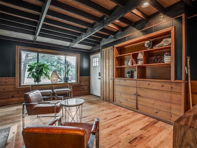 sitting room featuring light wood-style floors, wood walls, wainscoting, and beam ceiling
